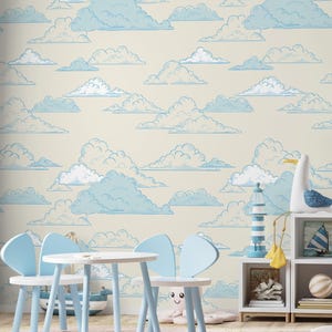 May include: A child's room with cloud-patterned wallpaper in light blue and cream. The room features a small white table and chairs, a white bookshelf with nautical decor, and a wooden floor. A lamp with a gold base sits on the bookshelf.