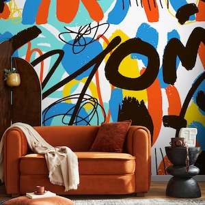 May include: An orange sofa with a throw blanket and decorative pillows sits in front of a wall with colorful abstract art. The art features bold strokes of blue, orange, yellow, and black against a white background. A small side table and decorative items complete the scene.