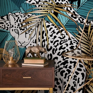 May include: A gold metal lamp with a cage-like shade sits on a dark wood nightstand. A gold metal sculpture of a bear sits on a stack of books. The background is a wallpaper with a black and white leopard print and gold and teal leaves.