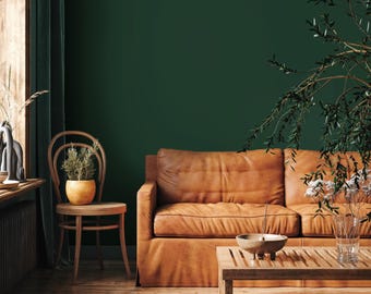 May include: A living room with a dark green wall and hardwood floor. A brown leather sofa and wooden coffee table are in the center. A wooden chair with a potted plant sits to the left. A vase of flowers and a plant are on the table.