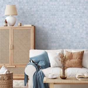 May include: A living room scene with a white sofa, blue and brown pillows, and a wooden coffee table. A woven cabinet and a lamp with a beige shade are on the left. The wall is decorated with a light blue triangle pattern.