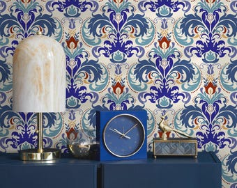 May include: A navy blue cabinet with a patterned wallpaper background. A marble-like lamp, a blue square clock, a glass bowl, a gold bird figurine, and a small glass box are on top of the cabinet. The wallpaper has a repeating floral design in blue, red, and gold.