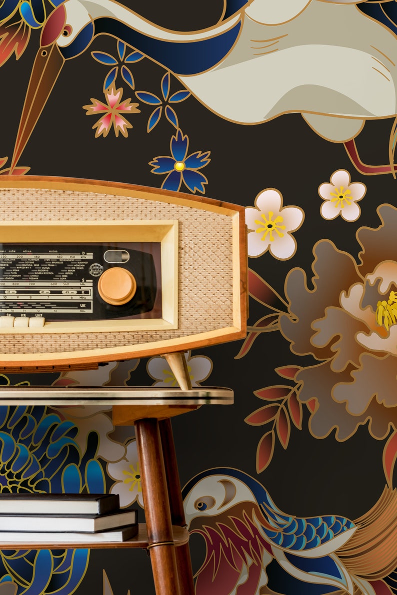 May include: A vintage-style radio with a woodgrain finish sits on a wooden table in front of a black background with a floral pattern. The pattern features cranes, flowers, and leaves in shades of blue, red, gold, and white.