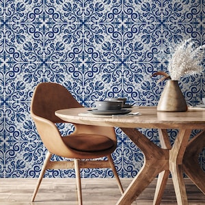 May include: A dining room scene featuring a round wooden table with a brown leather chair. The background is a wall with a blue and white ornate floral pattern. A vase with dried flowers and a gray bowl are on the table.