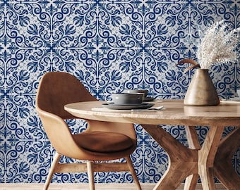 May include: A dining room scene featuring a round wooden table with a brown leather chair. The background is a wall with a blue and white ornate floral pattern. A vase with dried flowers and a gray bowl are on the table.