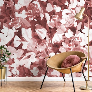 May include: A burgundy, white, and pink floral wallpaper with a watercolour effect. A tan leather chair with black legs and a round pink cushion is in front of the wallpaper. A gold floor lamp and a potted plant are also visible.