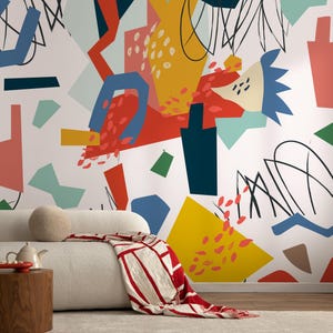 Könnte beinhalten: Ein modernes Wohnzimmer mit einem weißen Sofa, einem hölzernen Beistelltisch und einer rot-weiß gemusterten Decke. Die Wand zeigt ein farbenfrohes abstraktes Wandbild mit Formen in Rot, Gelb, Blau und Grün.