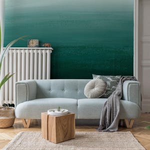 May include: A modern living room with a light blue sofa, wooden side table, and a woven rug. A green plant in a woven basket sits near the sofa. The wall is painted with a gradient of teal and green.