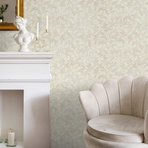 May include: A neutral-toned room featuring a white fireplace, a bust sculpture, and a gold-framed mirror. The wall is covered in a subtle, light-colored wallpaper with a delicate leaf pattern. A plush, light-colored armchair adds a touch of elegance.