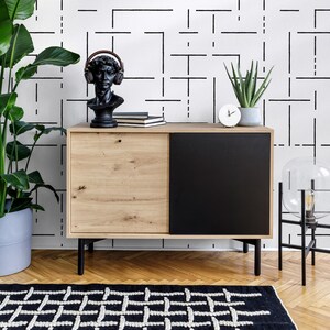 May include: A black and white geometric patterned wallpaper with a wooden cabinet with a black door. The cabinet is decorated with a bust of a person wearing headphones, books, and a small clock.