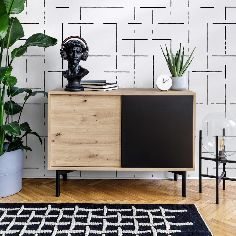 May include: A black and white geometric patterned wallpaper with a wooden cabinet with a black door. The cabinet is decorated with a bust of a person wearing headphones, books, and a small clock.