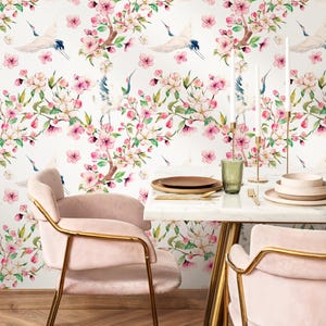 May include: A dining room scene featuring a white marble table set with plates, cutlery, and candles. Two pink chairs with gold frames are in the foreground. The wallpaper has a floral pattern with pink blossoms and cranes.