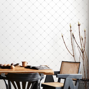 May include: A dining room scene featuring a wooden table with a black chair in the foreground. The white wall is adorned with a black diamond pattern. A cup, a book, and a bowl of fruit are on the table. Decorative branches are in the background.