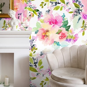 Puede incluir: Papel pintado floral acuarela con grandes flores rosas y amarillas, hojas verdes y detalles morados. El diseño está sobre un fondo blanco y es visible en una pared detrás de una chimenea blanca y un sillón beige.