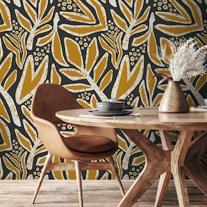 May include: A dining room scene featuring a round wooden table, a brown leather chair, and a vase with dried flowers. The background is a wallpaper with a black, gold, and white leaf pattern. A gray bowl and plate are on the table.