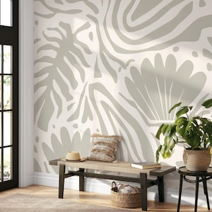 Pode incluir: Cena interior em tons neutros com um banco com assento tecido, uma almofada decorativa e um chapéu de palha. A parede é adornada com um padrão botânico abstrato em grande escala em tons de cinza e branco. Uma planta em vaso está numa mesa lateral.