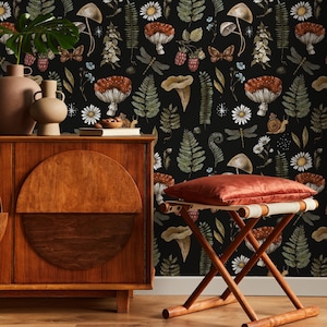 May include: A dark wallpaper featuring a repeating pattern of mushrooms, ferns, daisies, and butterflies. A wooden cabinet and a folding stool with a red cushion are in the foreground. The cabinet has a large, circular design on its door.