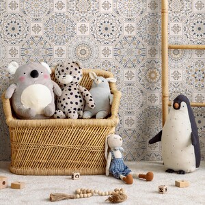 May include: A wicker storage bin filled with a variety of soft toys, including a koala, a leopard, a bunny, and a penguin. The bin is positioned in front of a wall covered in patterned wallpaper featuring hexagonal tiles with intricate designs in shades of blue, brown, and white.