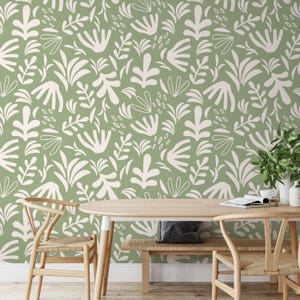 Pode incluir: Papel de parede verde sálvia com um padrão repetido de formas botânicas brancas. A imagem também mostra uma mesa de jantar de madeira, cadeiras e um banco. A mesa está decorada com alguns itens decorativos, incluindo uma planta e uma xícara de café.