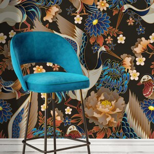 May include: A teal blue velvet bar stool with a black metal frame and gold accents. The stool is in front of a black background with a floral pattern featuring cranes, flowers, and birds.