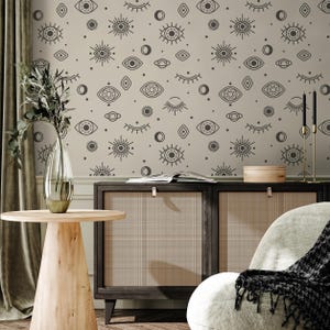 May include: A room interior featuring a beige wall with a repeating pattern of stylized eyes, moons, and suns. A wooden table with a vase of greenery sits in front of a dark wood cabinet. A chair with a patterned throw is in the foreground.