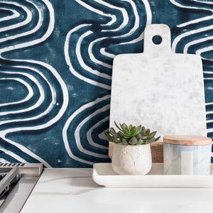 May include: A white marble cutting board with a hole, a small succulent in a white pot, and a decorative jar with a wooden lid sit on a white tray. The background features a blue and white abstract pattern.