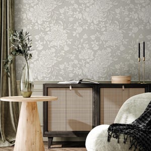 May include: An interior scene with light green floral wallpaper, a wooden side table, and a dark wood cabinet with woven panels. A clear glass vase holds greenery, and a gold candle holder with black candles is present.