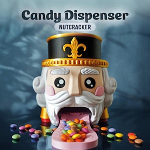 Puede incluir: Un dispensador de caramelos con forma de soldado cascanueces. El dispensador es de color beige, negro y dorado, con barba blanca y mejillas rosadas. El texto "Candy Dispenser NUTCRACKER" está en la parte superior. Los caramelos de colores se dispensan por la boca.