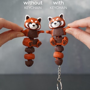 Könnte beinhalten: Zwei rote Panda-Figuren, eine mit und eine ohne Schlüsselanhänger, werden gezeigt. Die Figuren sind orange und braun mit weißen Akzenten. Der Text "without KEYCHAIN" und "with KEYCHAIN" steht über jeder Figur. Die Figuren werden von Händen gehalten.