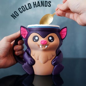 May include: A novelty mug shaped like a cartoon bat, predominantly purple with pink ears and a tan belly. The mug has the text "NO COLD HANDS" above it. A gold spoon is held over the mug.