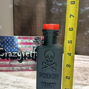 May include: A black glass bottle with a red cap and a skull and crossbones design. The bottle is labeled "POISON TINCT IODINE".