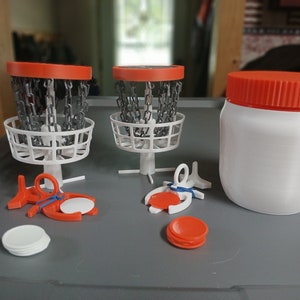 May include: A set of miniature disc golf baskets with orange rims and white bases, along with orange discs and a white container with an orange lid.