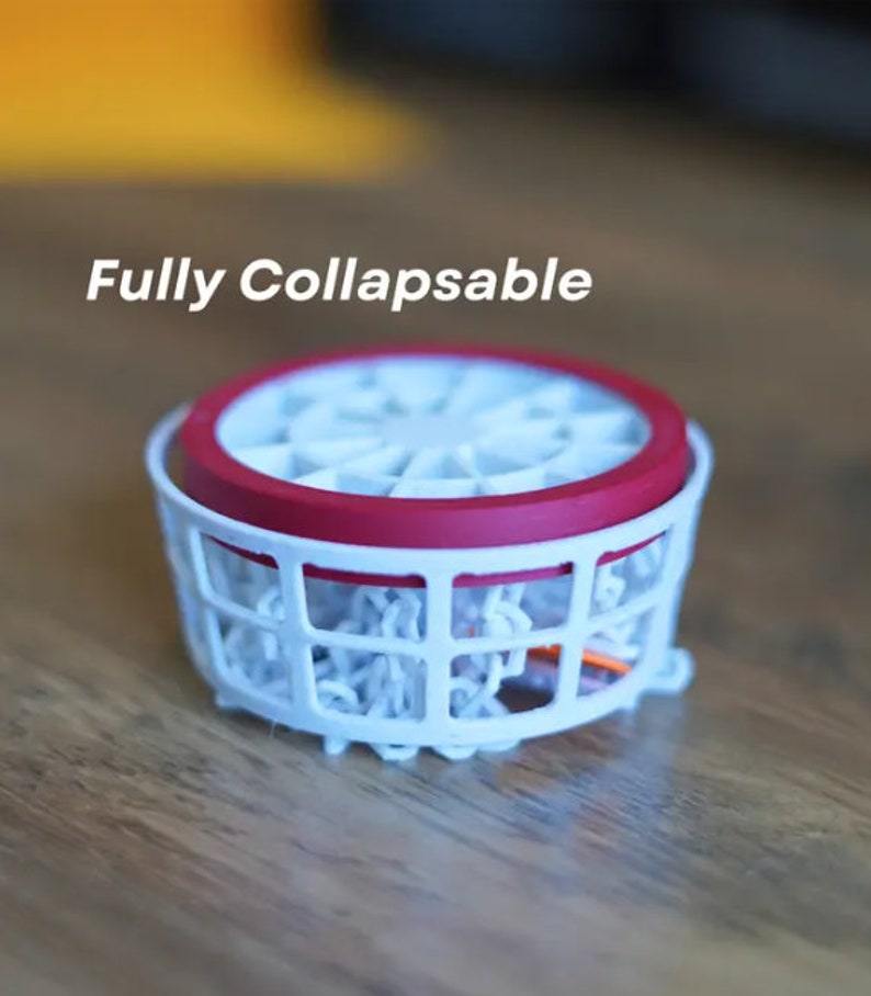 May include: A white collapsible basketball hoop with a red rim. The hoop is fully collapsed and is sitting on a wooden surface. The text "Fully Collapsible" is written above the hoop.