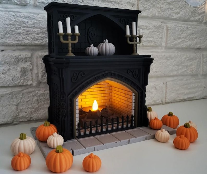 Puede incluir: Una chimenea negra con una vela encendida en su interior y un candelabro decorativo dorado con velas blancas en la parte superior. Hay varias calabazas peque&ntilde;as de color naranja y blanco delante de la chimenea.