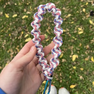 May include: A lanyard with a spiral design in white, red, and blue, with a blue carabiner clip. The pattern resembles the American flag. The lanyard is made of a tightly woven material.