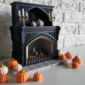 Puede incluir: Una chimenea de estilo g&oacute;tico negro con una rejilla de hierro decorativa y un hogar. La chimenea est&aacute; decorada con peque&ntilde;as calabazas blancas y velas. Hay varias calabazas peque&ntilde;as de color naranja en el suelo frente a la chimenea.