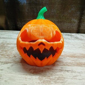 May include: An orange Halloween pumpkin with a carved scary face and a green stem. The pumpkin is sitting on a white wooden surface.