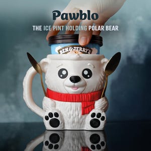 May include: A white ceramic polar bear mug with a red scarf, holding a pint of ice cream. The mug has a cartoon design with black paw prints and a black nose. The text "Pawblo" and "THE ICE PINT HOLDING POLAR BEAR" are visible.