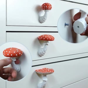 Może przedstawiać: Cztery białe, grzybowate uchwyty do szuflad z czerwonymi wierzchołkami i białymi kropkami. Uchwyty są przymocowane do białej komody.