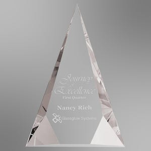 May include: A clear, triangular glass award featuring the etched text Journey of Excellence, First Quarter, Nancy Rich, and the Glassglow Systems logo. The award has faceted edges that create a prismatic effect, reflecting light across its surface.
