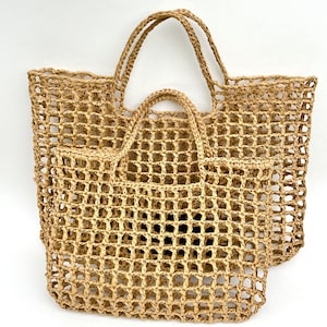 Può includere: Due borse tote in paglia intrecciata. La borsa più grande ha due manici e una forma rettangolare. La borsa più piccola ha un manico singolo e un motivo intrecciato simile. Entrambe le borse sono di colore beige naturale e hanno un design a griglia.
