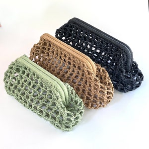 May include: Three woven clutch bags in shades of green, tan, and black. Each clutch has a rectangular shape with a woven net design and a curved top. The bags are made of a natural fiber material.