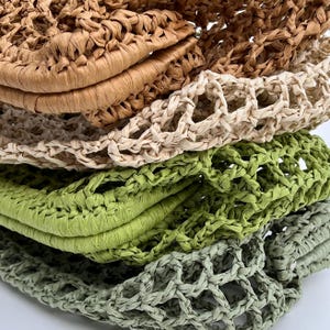 May include: A stack of four crocheted net bags made from paper-like material in shades of tan, cream, lime green, and sage green. Each bag features an open-weave mesh construction with a thick, folded edge and a textured, matte finish.