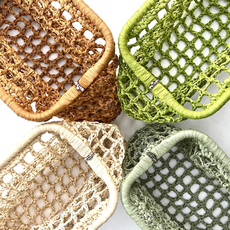 May include: Four rectangular baskets with an open grid weave pattern, each featuring a solid wrapped rim and a small silver-toned metal clasp. The baskets are colored in shades of tan, bright lime green, cream, and muted sage green.