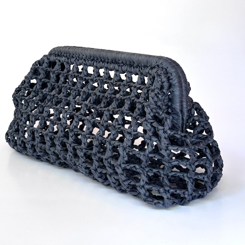 May include: A black clutch bag featuring a structured frame closure and an open, woven lattice design. The exterior is crafted from a textured, cord-like material, creating a repeating diamond pattern throughout the body of the handbag.