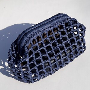 Puede incluir: Un bolso de mano azul oscuro con una estructura r&iacute;gida y un dise&ntilde;o de red tejida con cuadr&iacute;cula abierta. El exterior est&aacute; hecho de un material texturizado similar a una cuerda y contiene un objeto rectangular oscuro visible a trav&eacute;s de la malla.