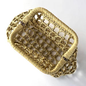 May include: A rectangular basket with an open-weave design made from light tan, natural-colored fibers. The basket features a sturdy, wrapped rim and two metal hinges on the sides, allowing the top frame to fold down against the body.