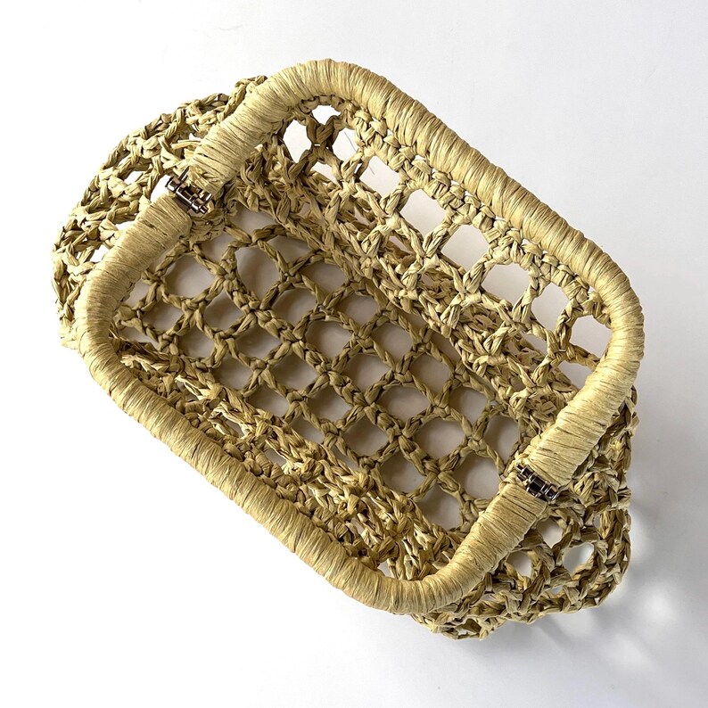 May include: A rectangular basket with an open-weave design made from light tan, natural-colored fibers. The basket features a sturdy, wrapped rim and two metal hinges on the sides, allowing the top frame to fold down against the body.
