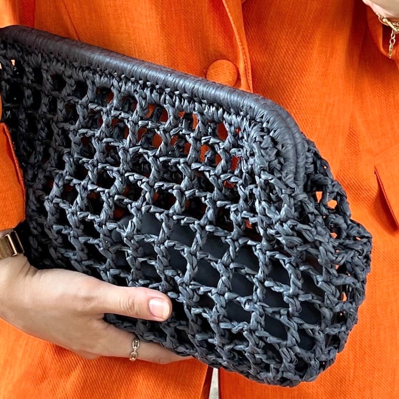 Puede incluir: Un bolso de mano color gris carb&oacute;n oscuro con un dise&ntilde;o de celos&iacute;a abierta y tejida, hecho de un material texturizado similar a una cuerda. El bolso rectangular tiene una abertura de marco estructurada y una bolsa interior negra lisa.