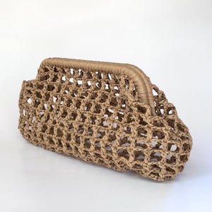May include: A beige clutch bag crafted from woven paper straw material. The bag features an open, lattice-style grid pattern throughout the body and a solid, tightly wrapped frame along the top edge, creating a structured, rectangular silhouette.